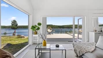Un salon moderne avec une table basse en verre, un canapé et une vue sur un lac et une forêt.