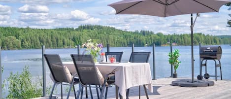Una terraza con mesa y sillas, una parrilla y vistas a un lago y bosque.