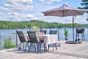 A deck with a table and chairs, a grill, and a view of a lake and forest. - Lakeside cabin on its own peninsula—completely secluded (hällefors)