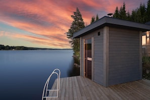 A wooden dock with a metal ladder leading to a small cabin by a calm lake at sunset. - Lakeside cabin on its own peninsula—completely secluded (hällefors)