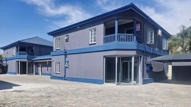 Un edificio de dos pisos con fachada azul, un balcón y una entrada a nivel de calle con puertas de vidrio.