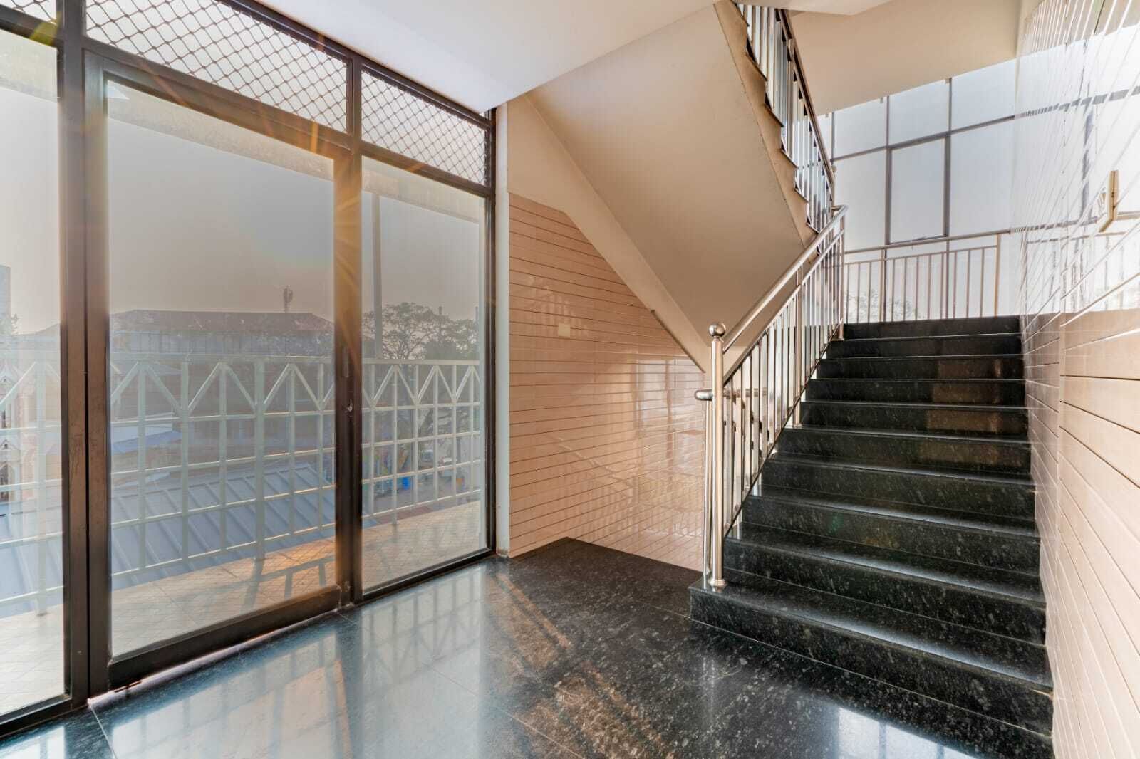 Un interior moderno con una escalera, una puerta de vidrio que da al exterior y vistas de una edificación.