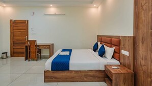 A hotel room with a bed, bedside table, wooden wardrobe, desk, chair, and a small trash bin. - Chaithanya Residency  (Kochi)