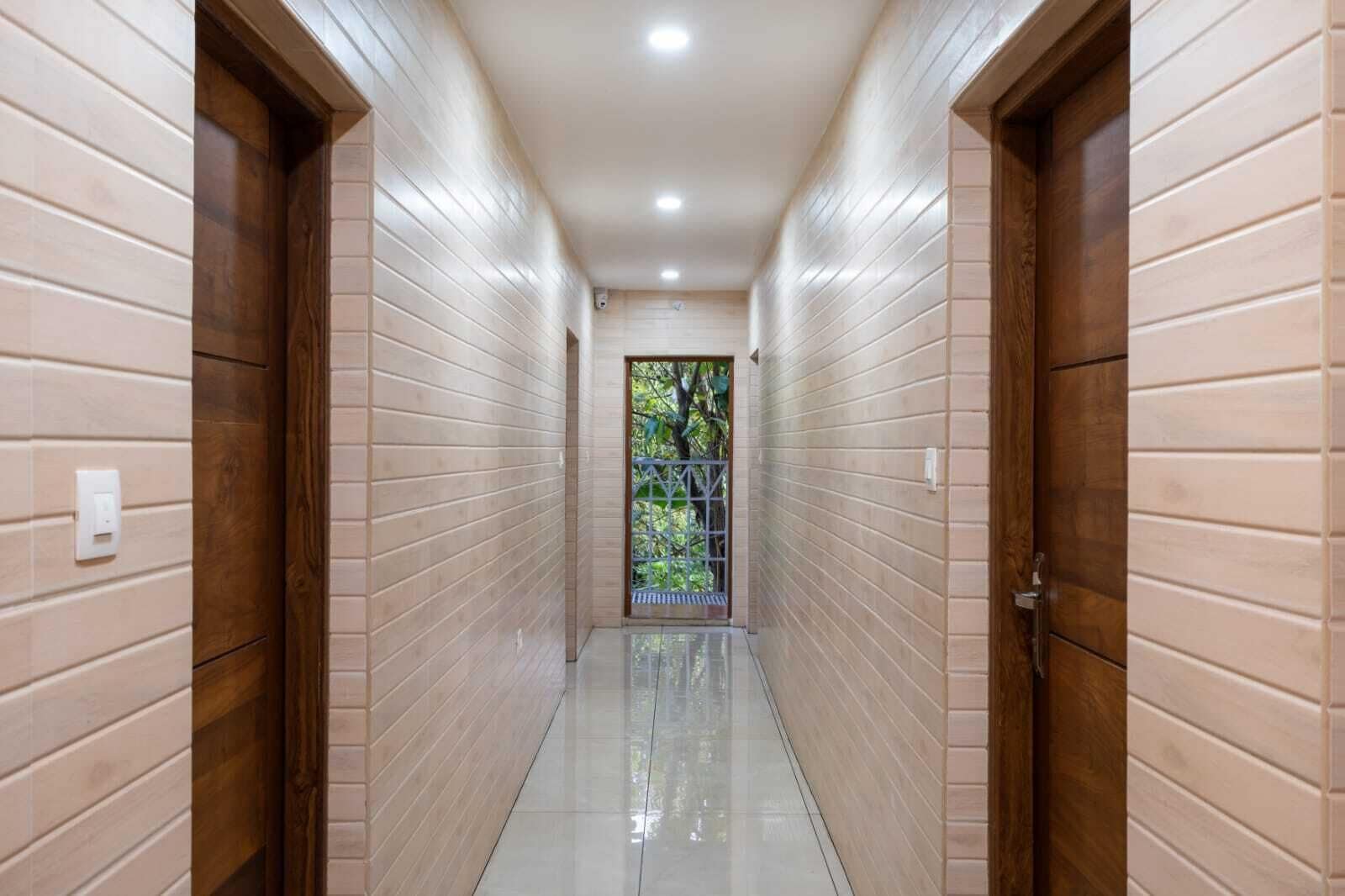 Un pasillo con puertas de madera y paredes de tonos claros, que conduce a una puerta con vistas al verdor.
