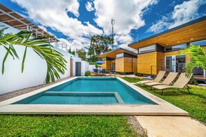 Ein moderner Poolbereich im Freien mit blauem Himmel, einer Holzterrasse und einer weißen Wand.