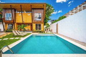 Ein modernes, zweistöckiges Gebäude mit Schwimmbad, Sitzgelegenheiten im Freien und einem gepflegten Garten.