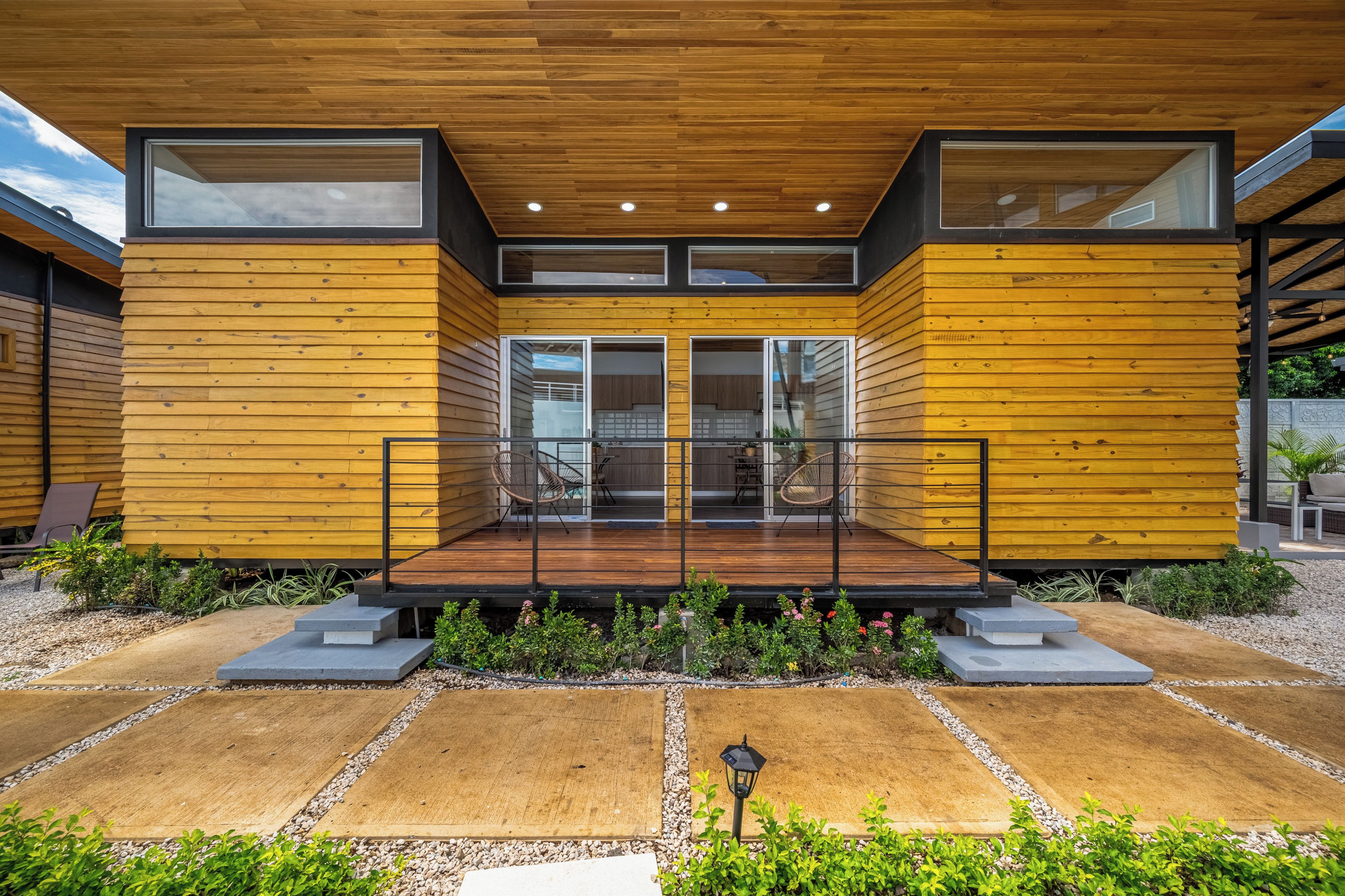Une maison moderne avec une façade en bois, de grandes fenêtres et un patio couvert.