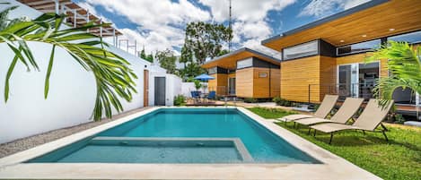 A modern outdoor pool area with a wooden deck, lounge chairs, and a clear blue sky.