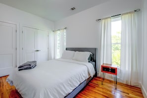 Un dormitorio con una cama, una mesita de noche, una ventana con cortinas y una puerta.
