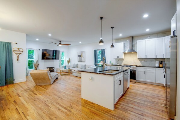 Una cocina moderna con armarios blancos, una isla central y una zona de comedor con un sofá y televisor.