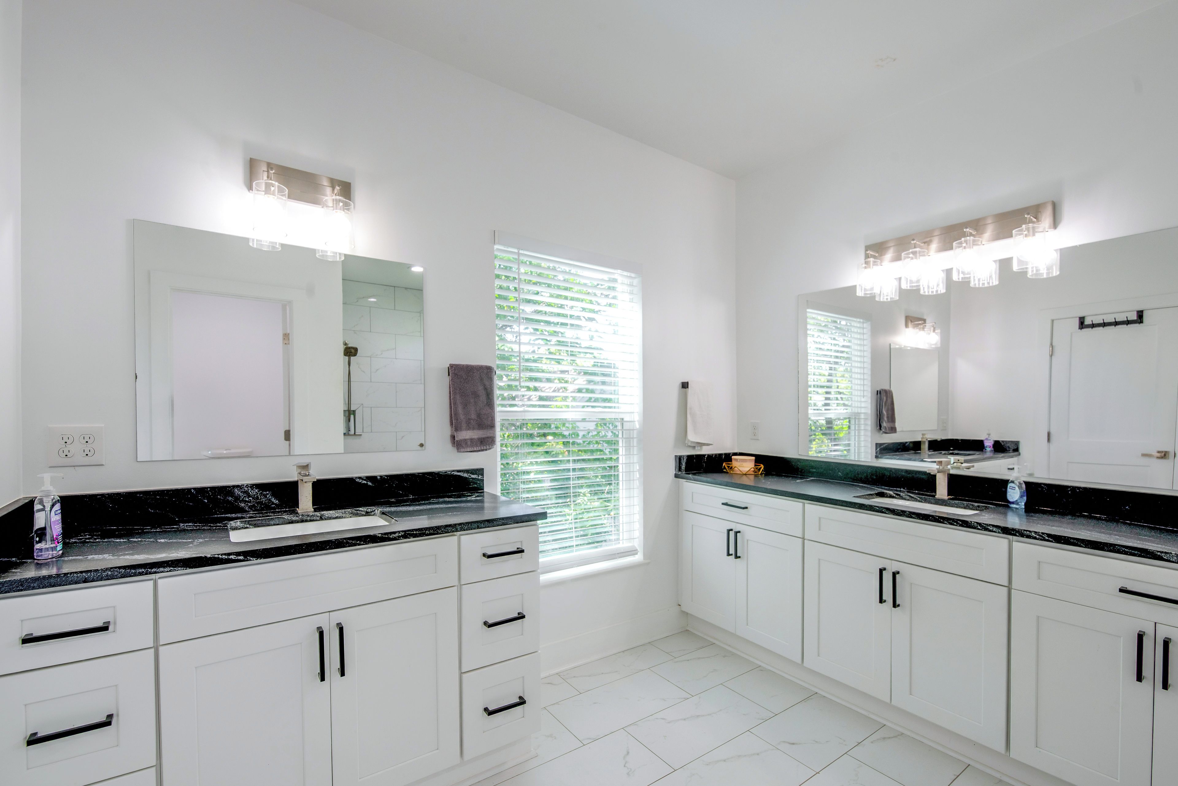 A modern bathroom with white cabinetry, a black countertop, and a large mirror above the sink.