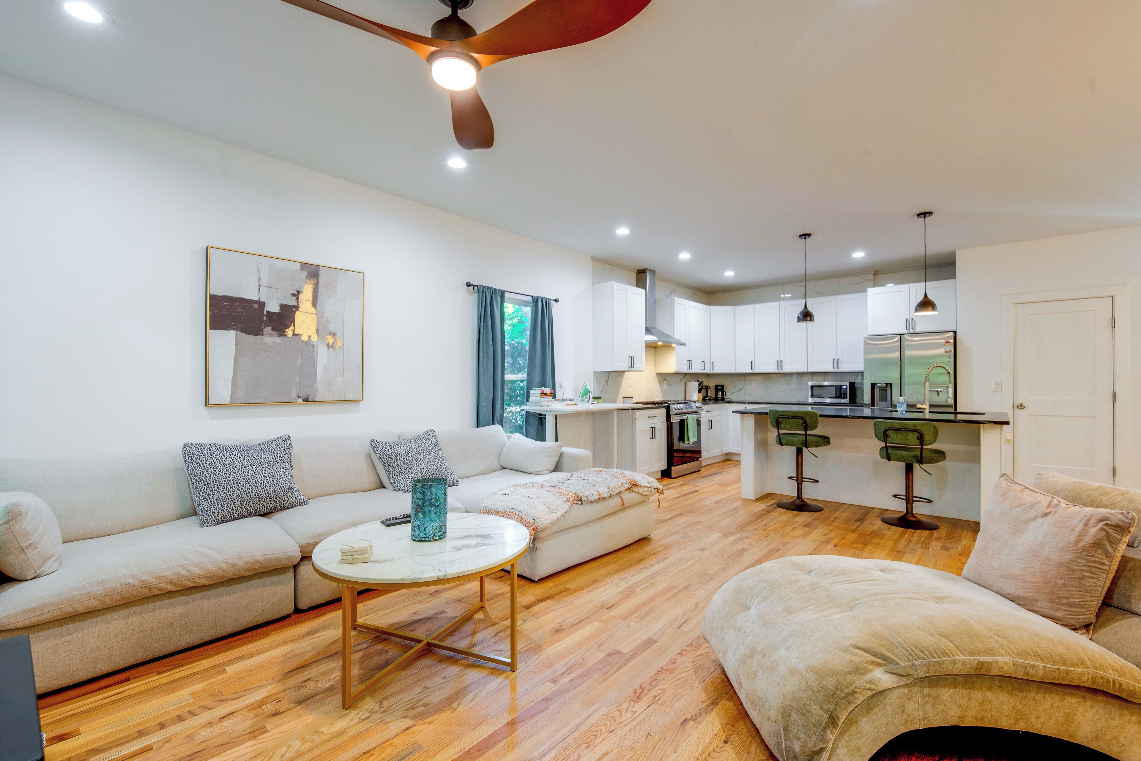 A modern living room with a sofa, a coffee table, and a kitchen area with a refrigerator, microwave, and bar stools.