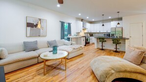 Una sala de estar moderna con un sofá, una mesa de centro y una zona de cocina con refrigerador, microondas y taburetes de bar.