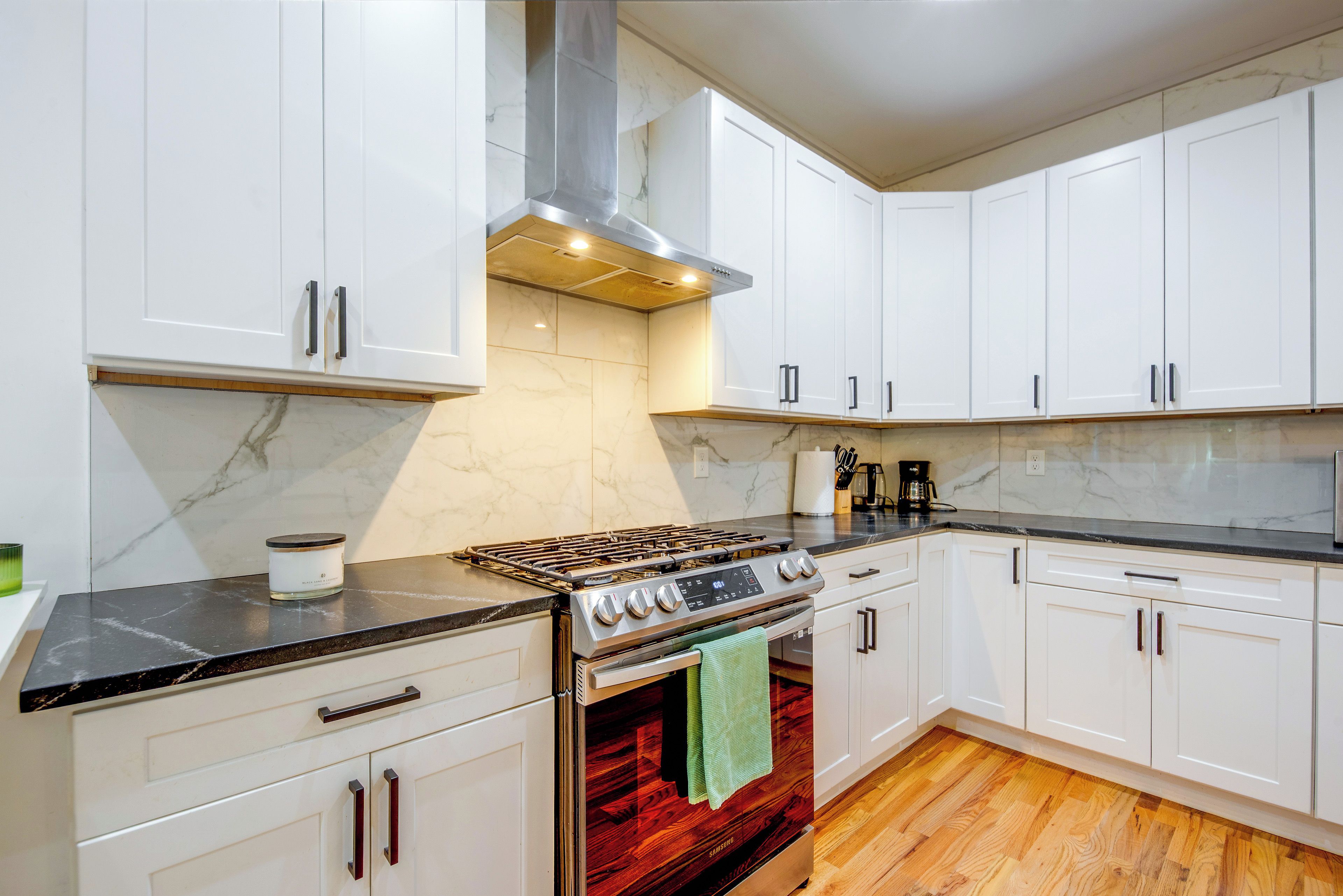 A kitchen with white cabinets, a stainless steel stove, and a wooden floor.