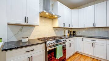 A kitchen with white cabinets, a stainless steel stove, and a wooden floor.