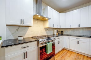 Cocina con armarios blancos, estufa de acero inoxidable y piso de madera.
