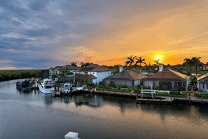 Een jachthaven met huizen en boten, een rustig wateroppervlak en een ondergaande zon op de achtergrond.