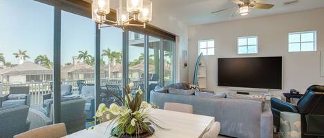 A spacious living room with a large TV, comfortable seating, and a balcony with a view.