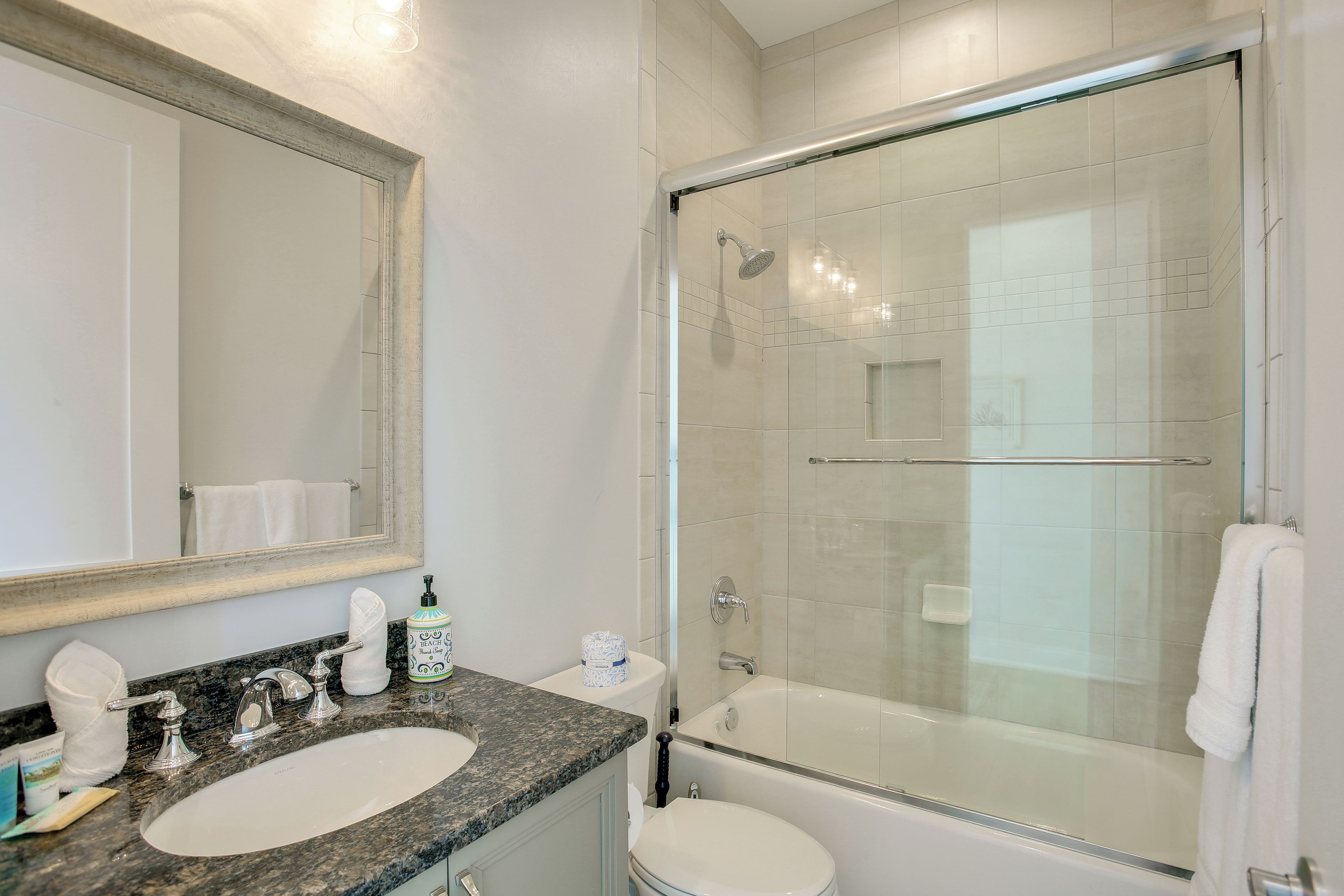 A bathroom with a granite countertop sink, a toilet, a shower with a glass door, and a mirror.
