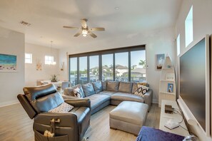 Een moderne woonkamer met een modulaire bank, een fauteuil, een flatscreen-televisie en een groot raam met uitzicht op de omgeving.