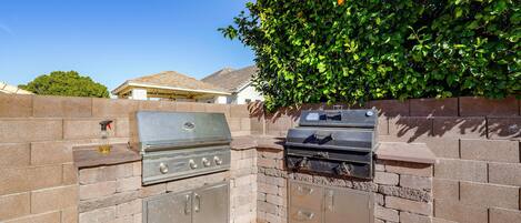 An outdoor kitchen with a grill and a built-in oven, surrounded by a brick wall and a tree.