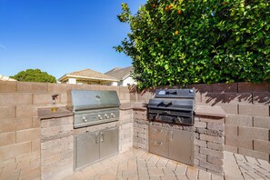 An outdoor kitchen with a grill and a built-in oven, surrounded by a brick wall and a tree.