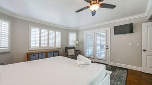 Quarto com cama, ventilador de teto, televisão e porta.