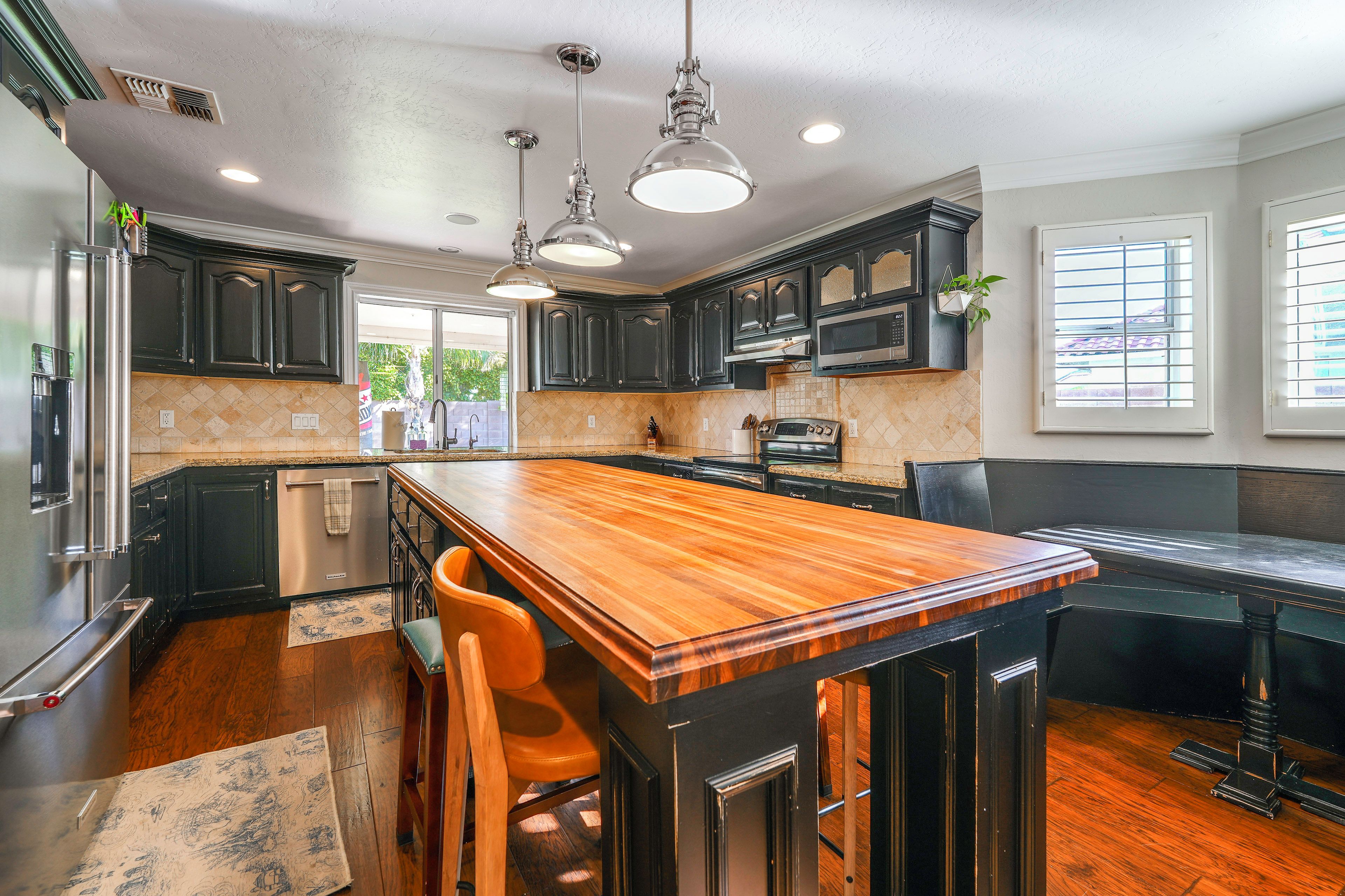 A modern kitchen with dark cabinetry, a wooden island, stainless steel appliances, and pendant lighting.