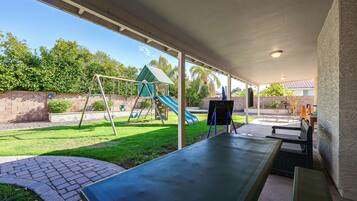 A covered patio area with a swing set, a slide, and a seating area with benches.