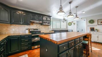 A kitchen with dark cabinetry, a central island, stainless steel appliances, and pendant lighting.