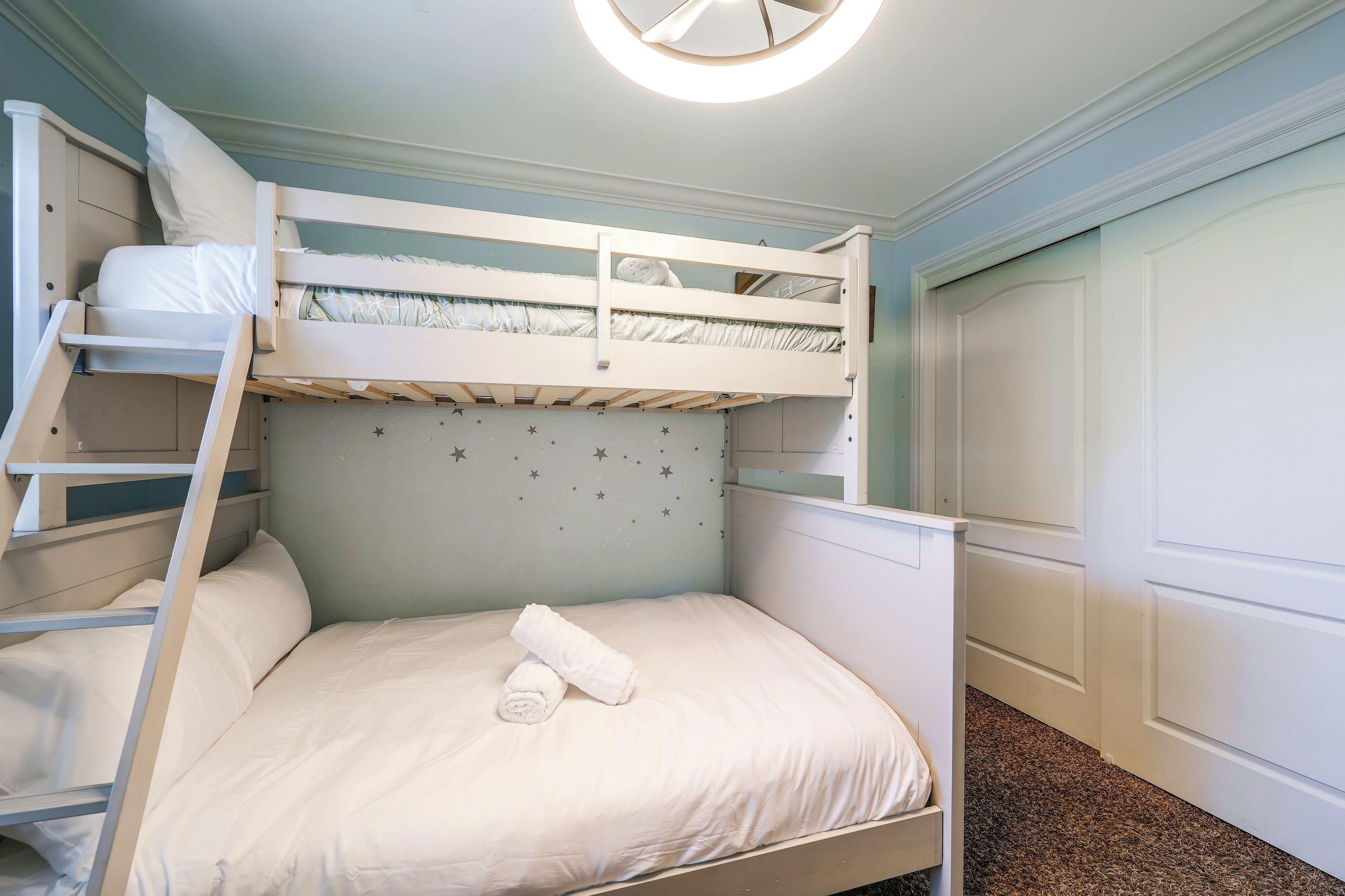 Une chambre avec un lit superposé, une échelle, une porte et un sol recouvert de moquette.