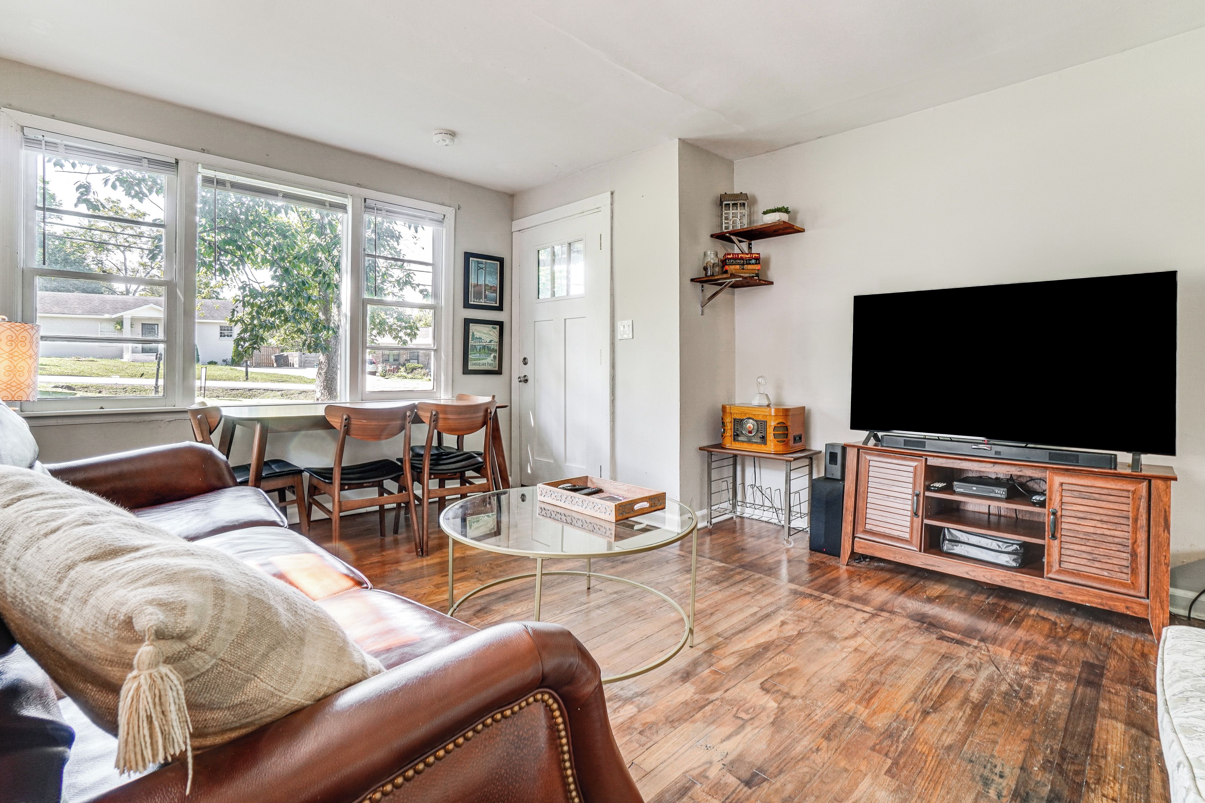A living room with a leather sofa, a glass coffee table, a flat-screen TV, and a wooden entertainment unit.