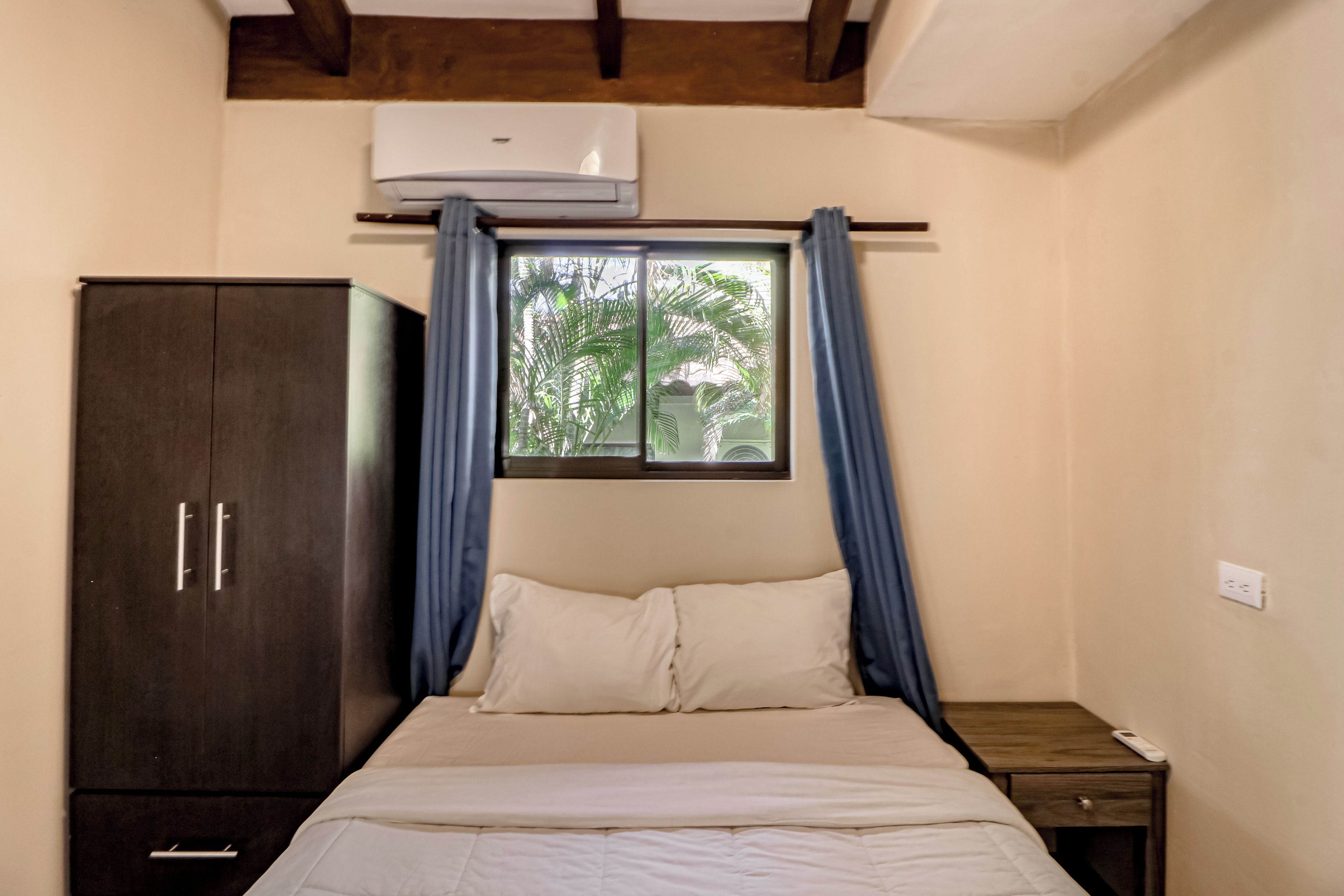 A bedroom with a bed, a wardrobe, a window with curtains, and a bedside table.