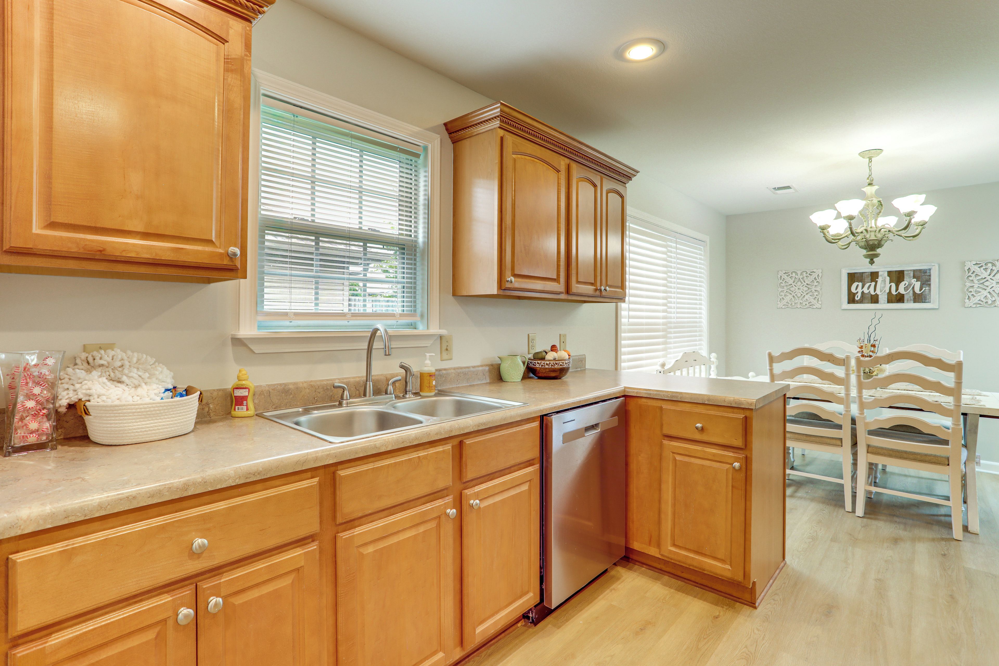 A kitchen with wooden cabinets, a dishwasher, a double sink, and a dining area with a white table and chairs.