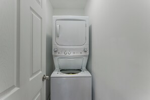 Máquina de lavar roupa compacta e branca, de abertura frontal, numa lavanderia pequena com porta fechada.