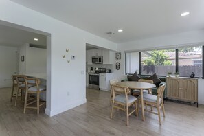 Cozinha moderna com armários brancos, micro-ondas e forno. Há uma área de refeições com cadeiras de madeira e uma mesa.