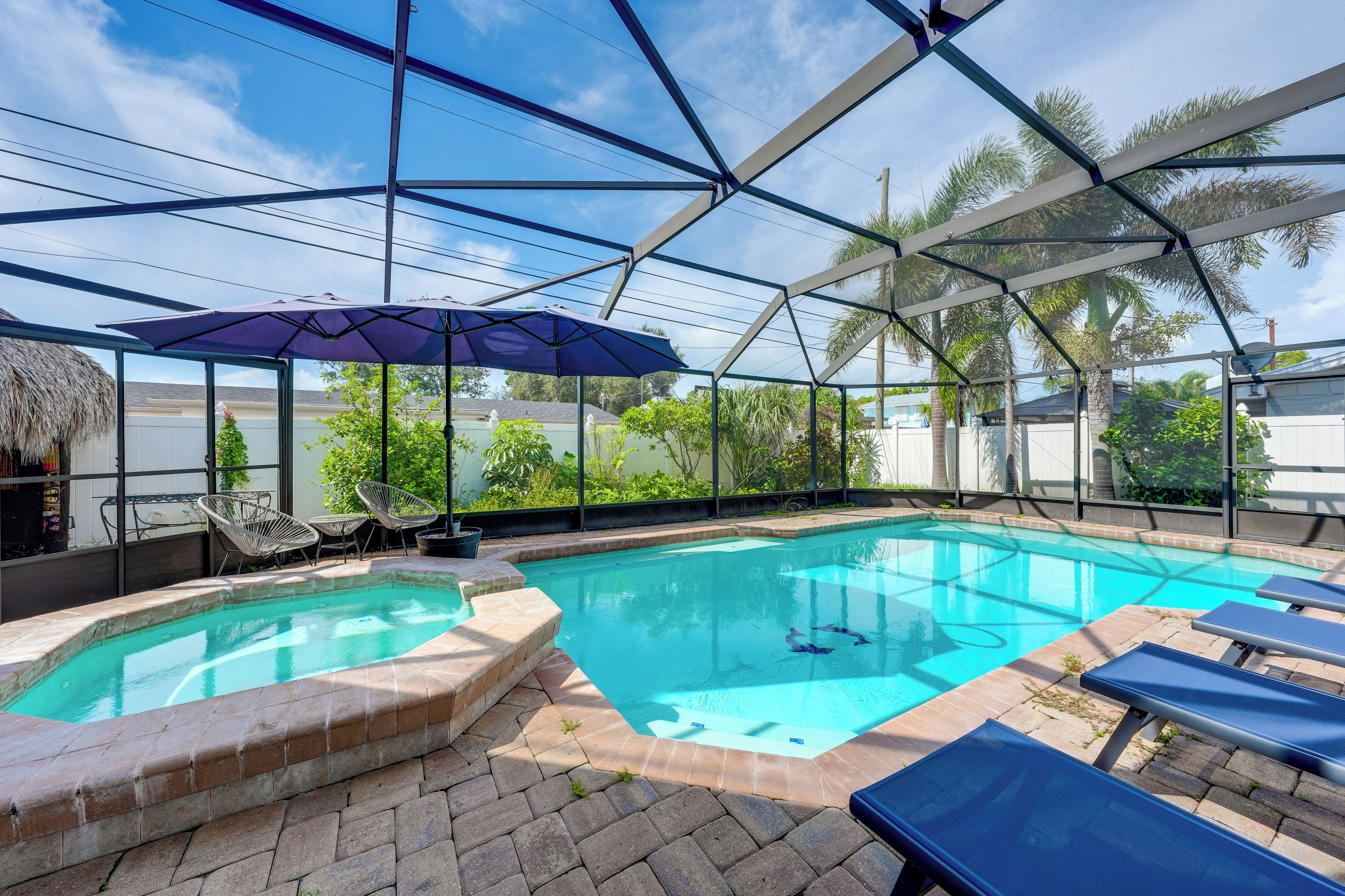 An indoor swimming pool with a glass enclosure, surrounded by lounge chairs and a thatched roof structure.