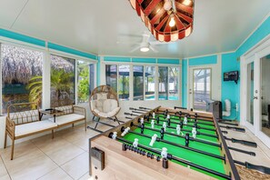 A room with a foosball table, a wicker chair, and a large window overlooking a pool. - 2 Mi to Redington Beach! Tropical Poolside Retreat (Seminole)