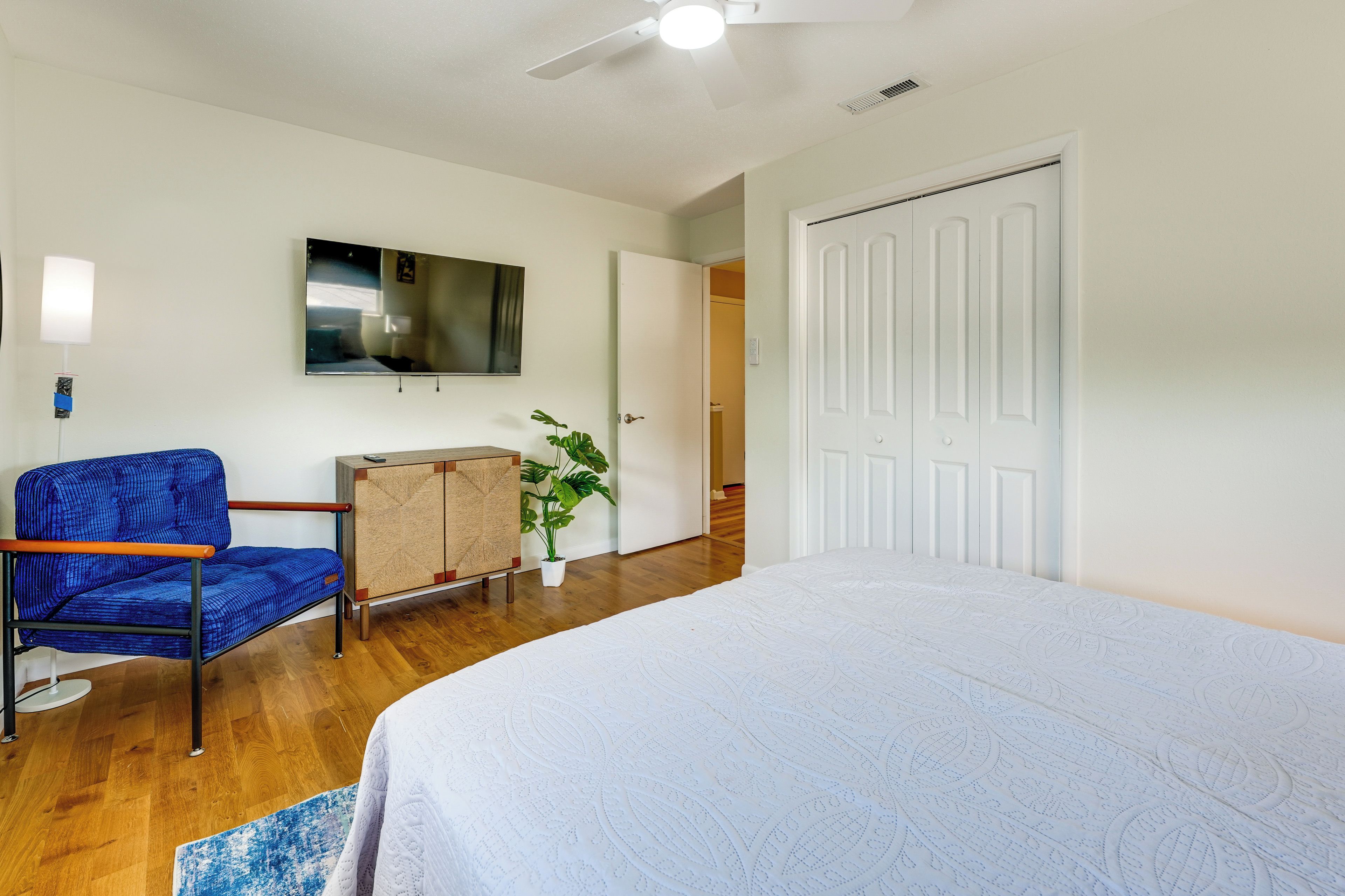 A bedroom with a bed, a chair, a television, a plant, and a wardrobe.