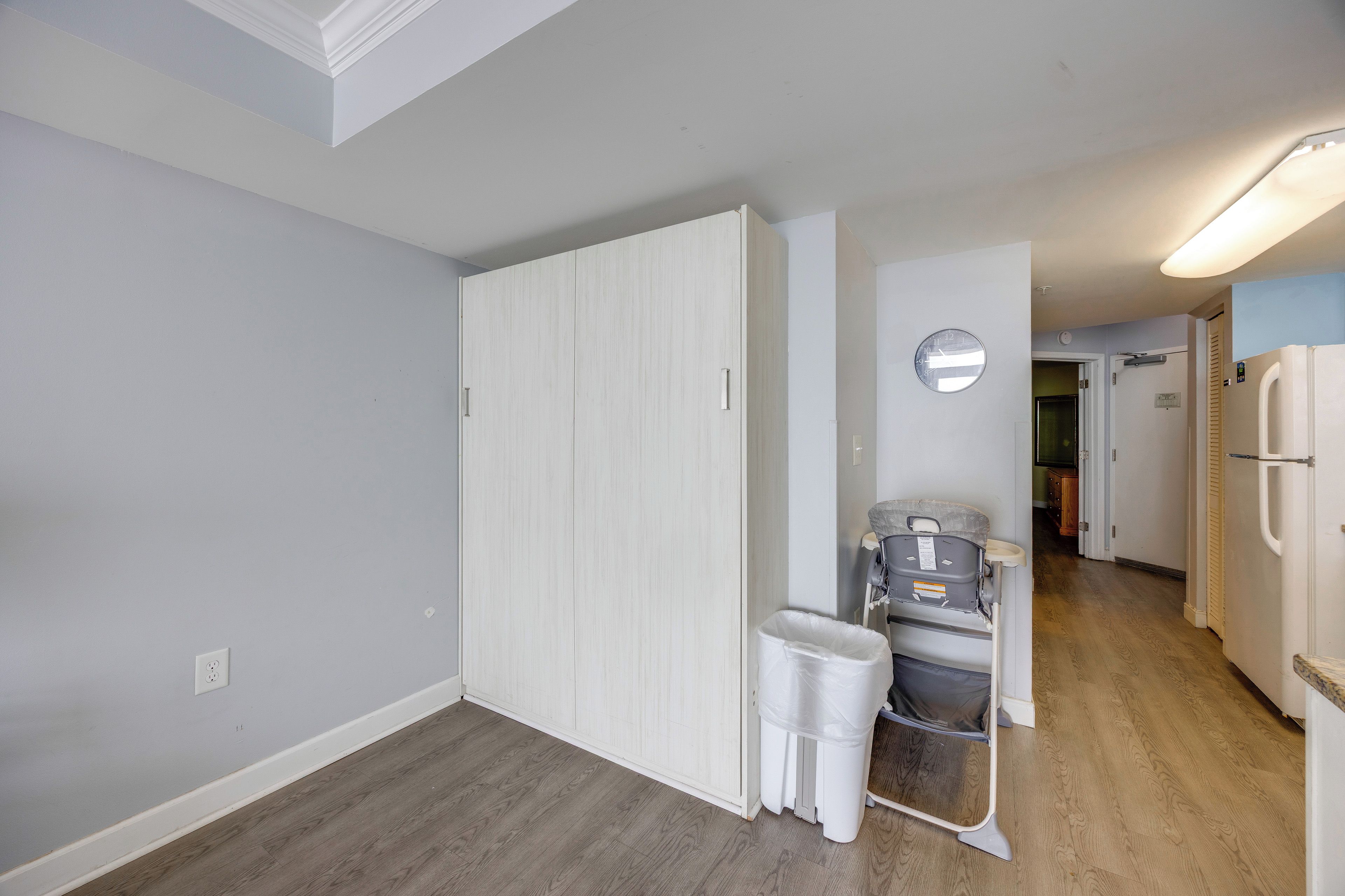 A hallway with a white door, a trash bin, a baby stroller, and a refrigerator.