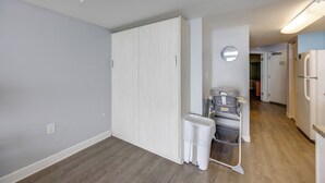 Een gang met een witte deur, een prullenbak, een kinderwagen en een koelkast.