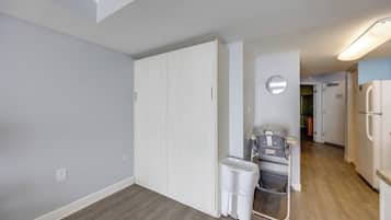 A hallway with a white door, a trash bin, a baby stroller, and a refrigerator.