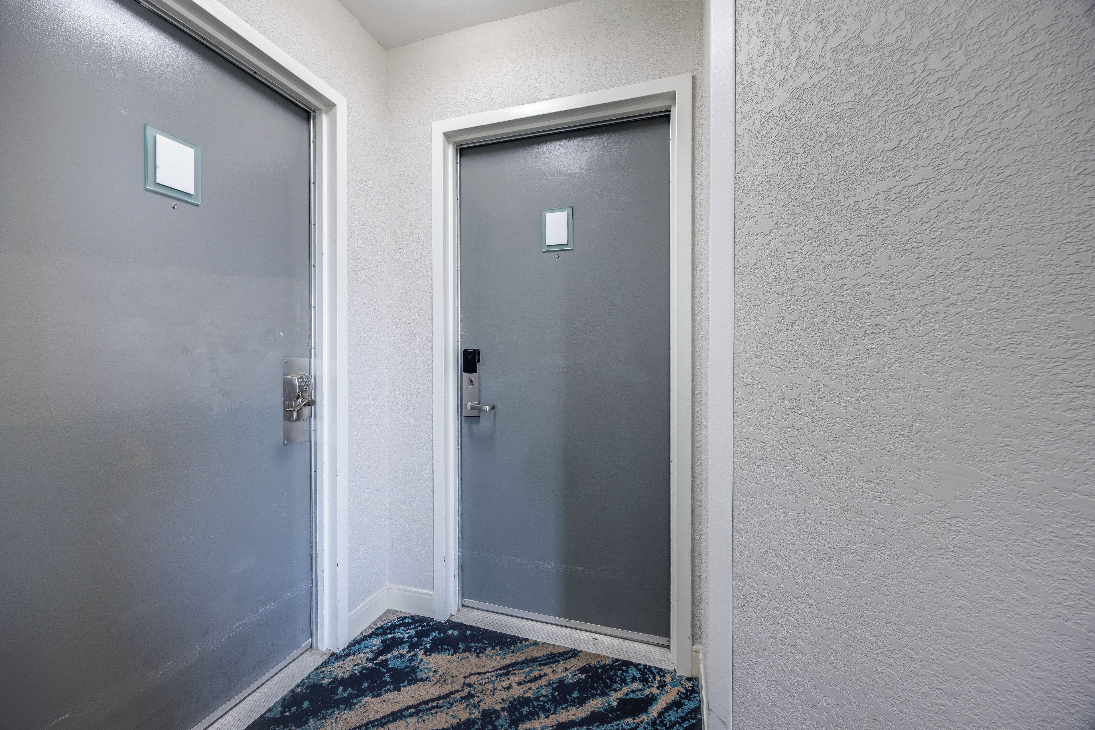 A hallway with two doors, one with a peephole and a handle, and the other with a doorbell.