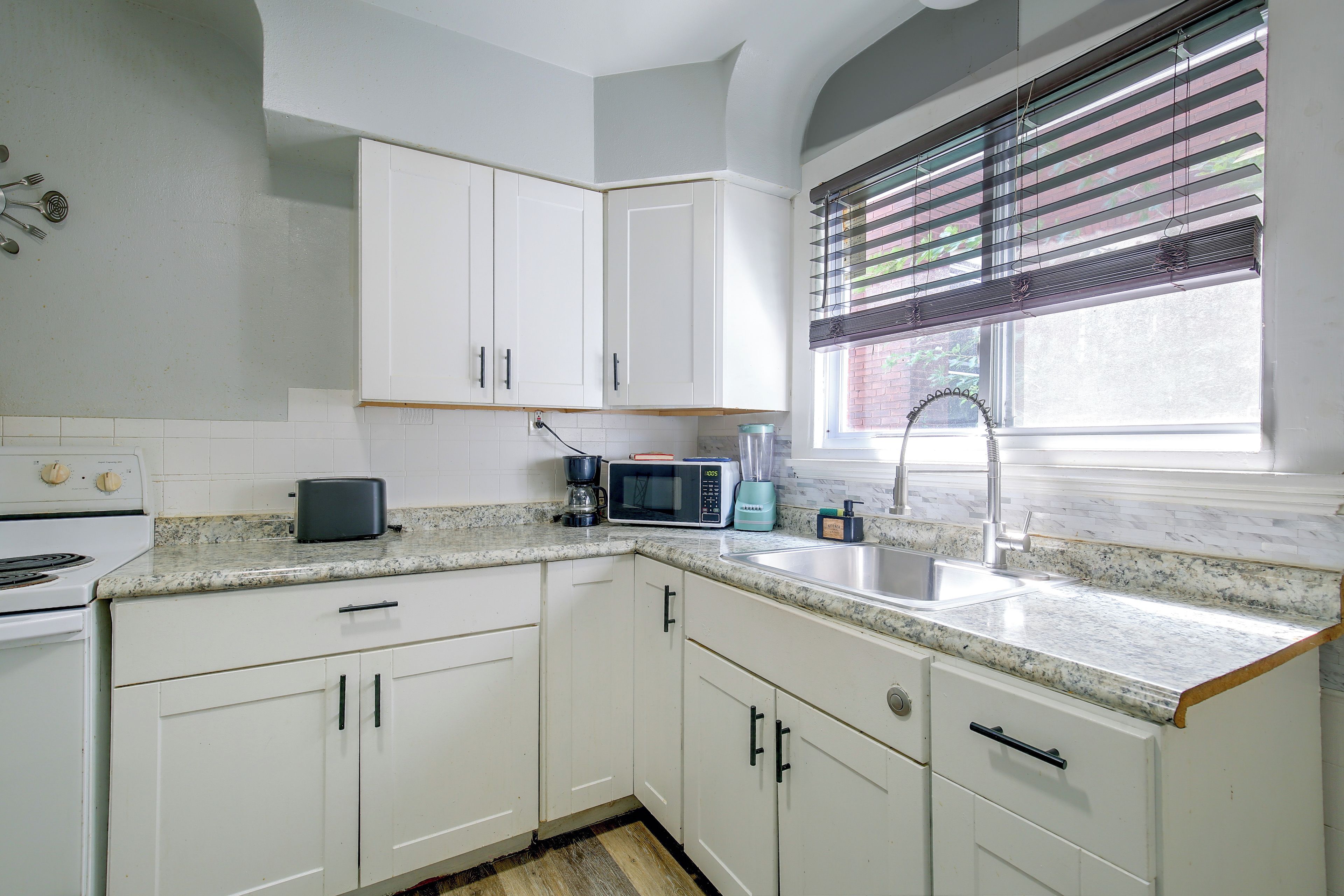 A kitchen with white cabinets, a microwave, a toaster, and a sink.