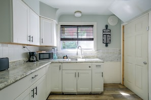 A kitchen with white cabinets, a microwave, a coffee maker, and a window with blinds. - Family Apt 7 Mi to Gateway Arch, Museums & More! (St. Louis)