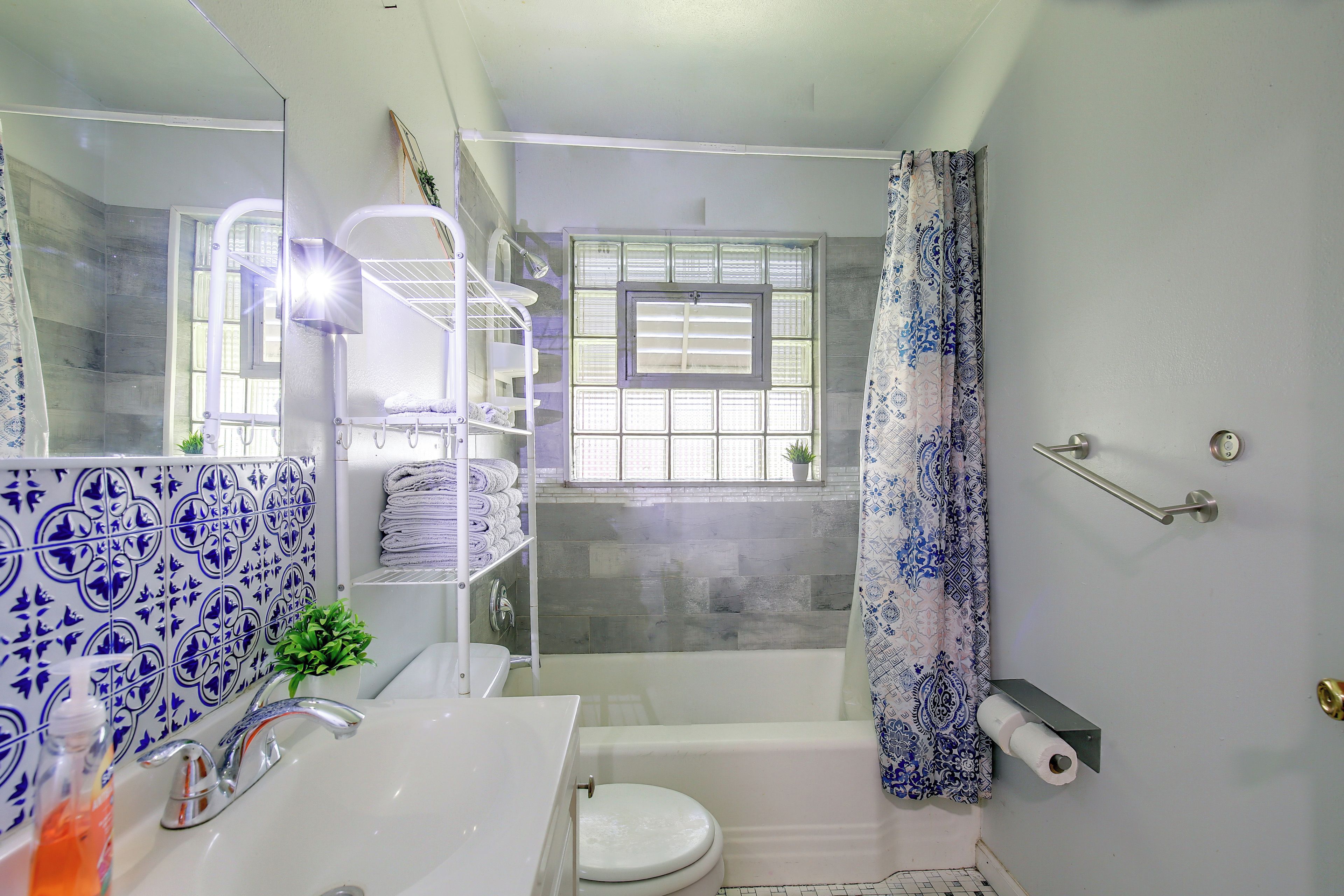 Un baño con lavamanos blanco, inodoro, zona de ducha y ventana con persianas.