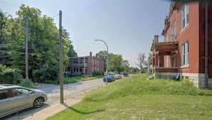 Eine Wohnstraße mit parkenden Autos, einer Grünfläche und einem rotziegelbau mit Balkon.