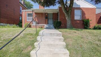 A residential house with a brick exterior, a front porch, and a concrete staircase leading to the front door.