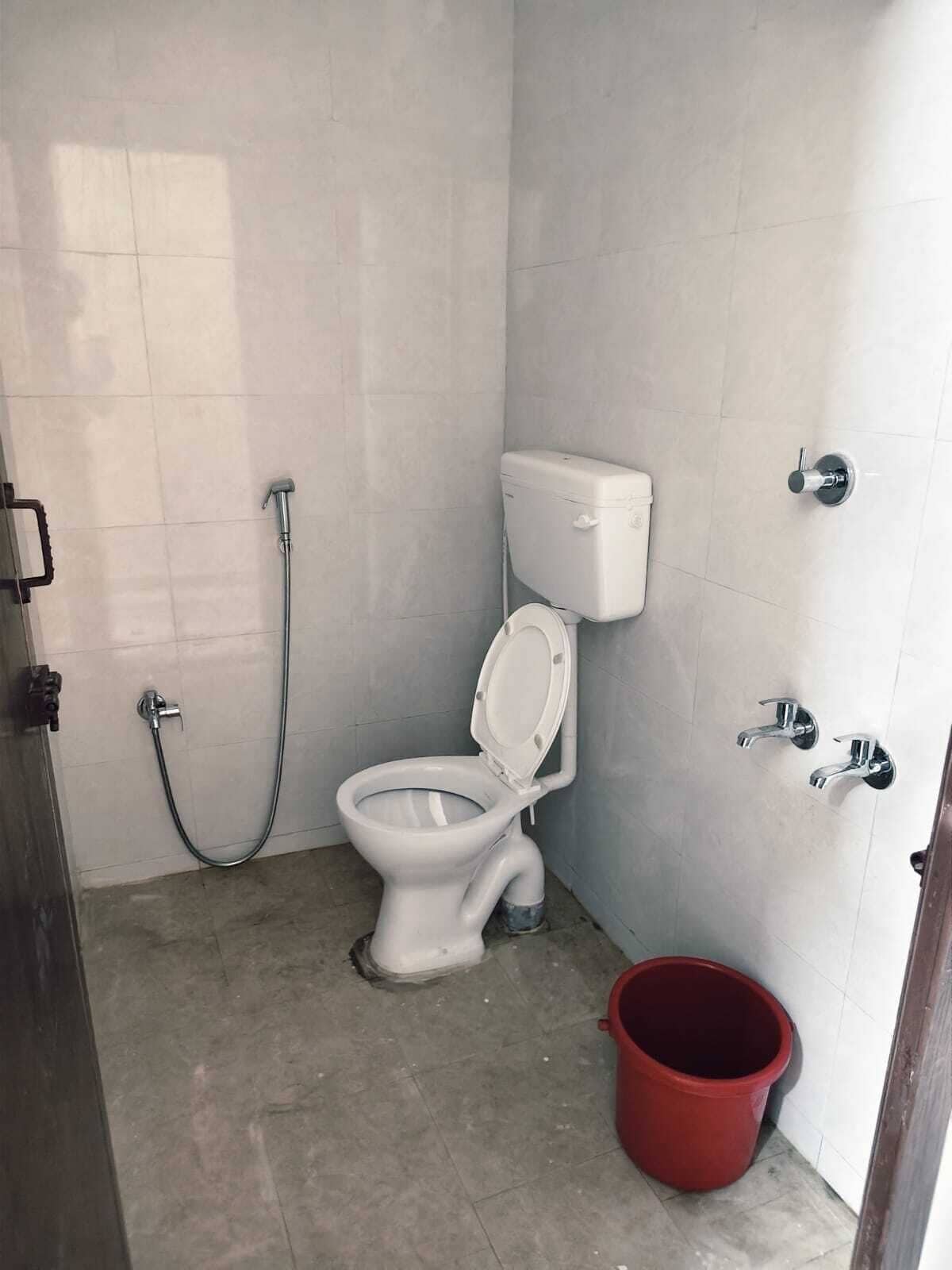 A bathroom with a toilet, a shower, and a red bucket.