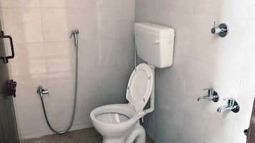 A bathroom with a toilet, a shower, and a red bucket.